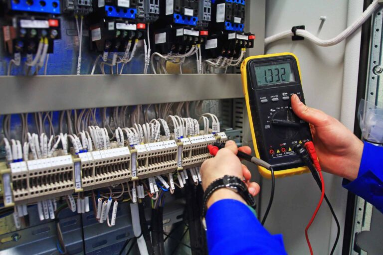 Engineer testing industrial electrical circuits with a multimeter in a control terminal box